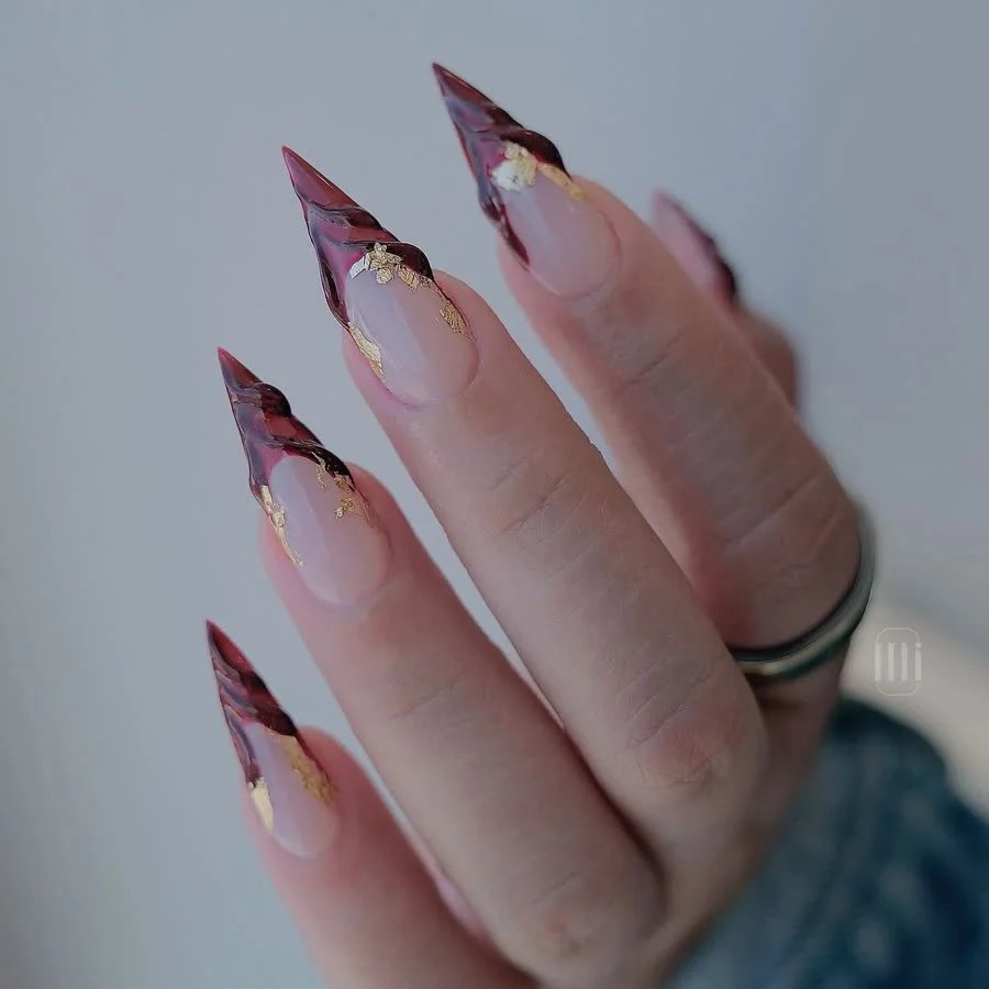 Sculpted stiletto nails with deep wine tips and gold leaf